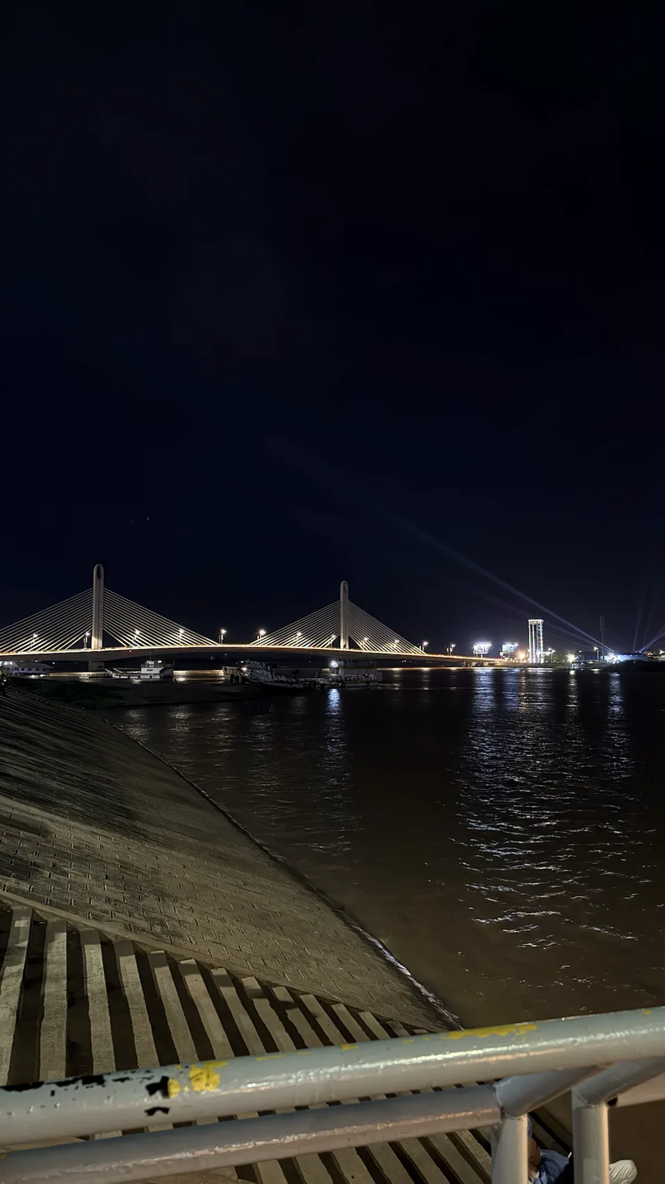 Подсвеченный вантовый мост над рекой, вид с набережной ночью